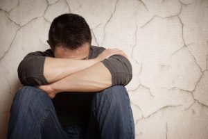 A man experiencing emotional pain sat on the floor and leaning against a wall