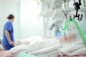 A patient in a bed and a nurse in the background.