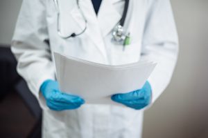 A doctor with blue gloves holding medical papers.