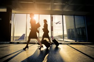 Two women walking through an airport with their suitcases.