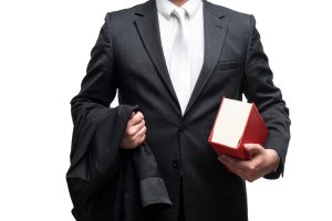 A male personal injury solicitor holding his blazer jacket in one arm and a red law book in the other.