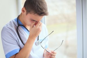 A doctor holds his glasses in one hand and pinches his nose with the other after a patient suffered a pulmonary embolism