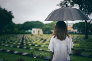 YOUNG WOMAN AT GRAVESIDE HOLDING AN UMBRELLA.