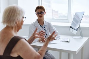 A medical professional sat on her desk talking to a patient.